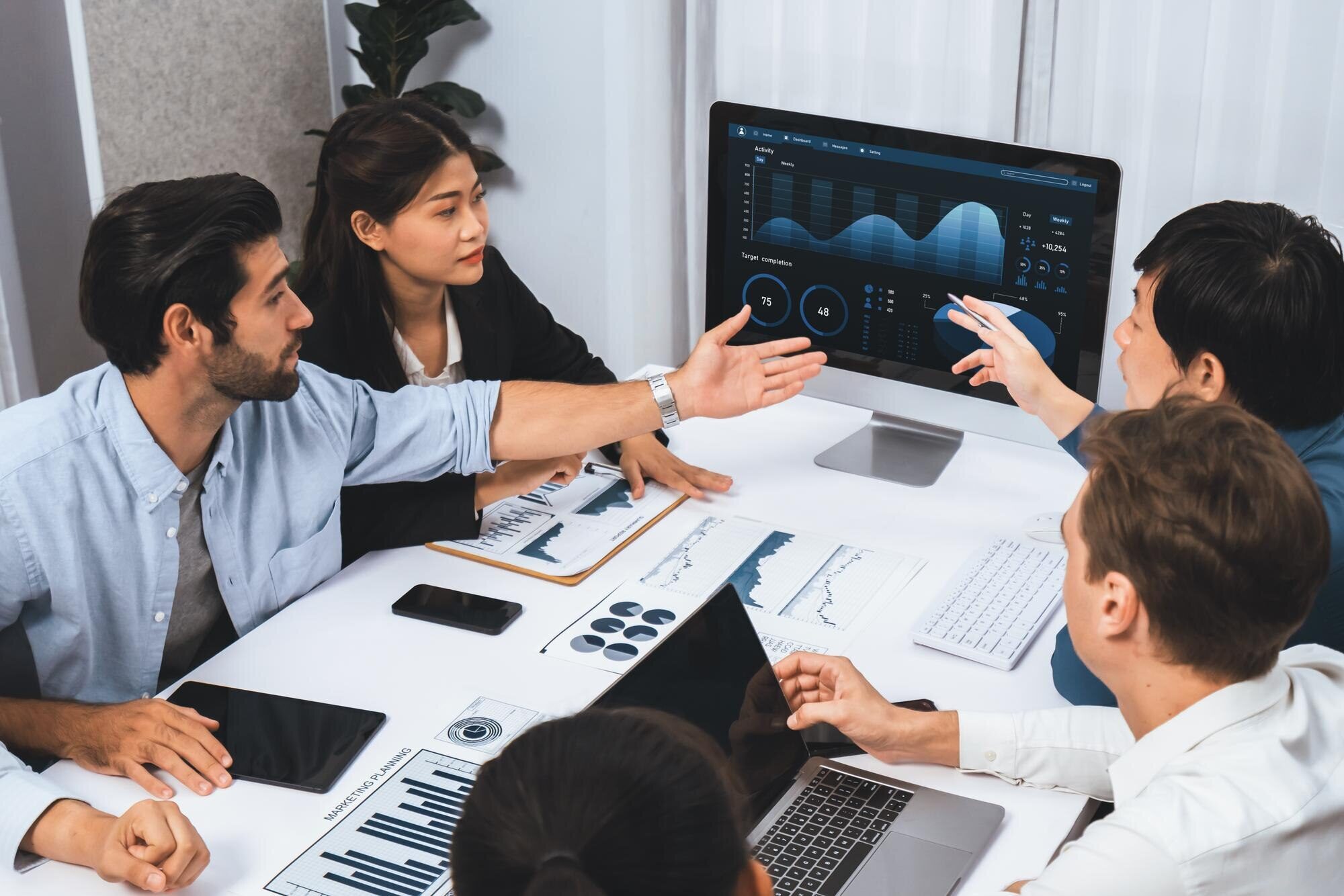 Kautilyam team of software consultants collaborating in a modern office, analyzing data visualizations on a computer screen and discussing strategies for software solutions.