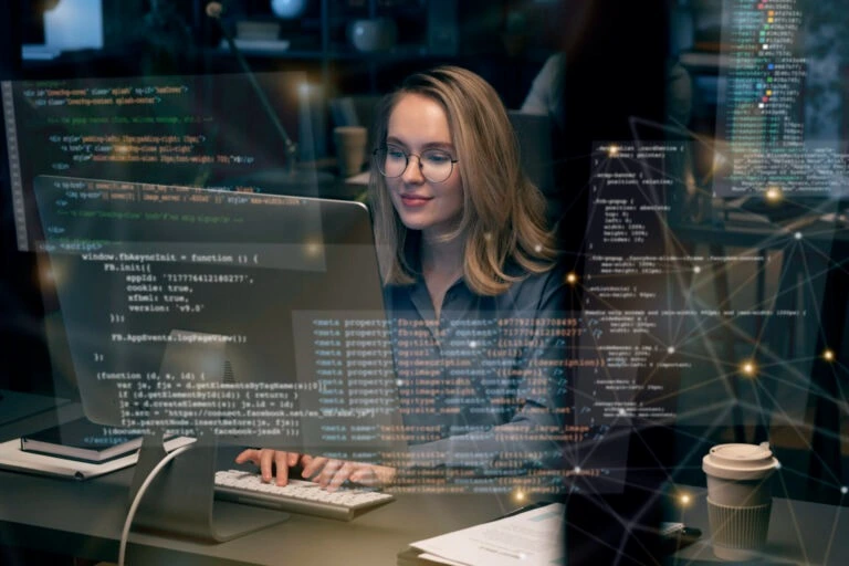 Woman working on computer with code overlay, representing website redesign services by Kautilyam for modern businesses.